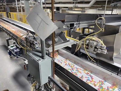 A belt conveyor drops candy into a diverter bucket that swings back and forth to feed belt conveyors that run in opposite directions, each feeding a pair of baggers.