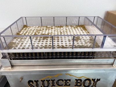 The filling system consists of two cartridges that sit atop a vibratory table that gently vibrates ground flower from the upper cartridge into the cone wrapping papers in the lower cartridge.