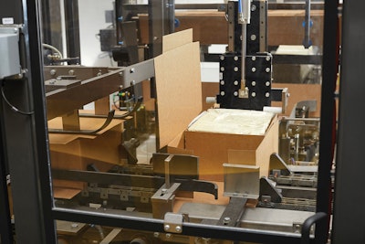 The automated system pushes cheese blocks into wraparound corrugated cases, which are then sealed and palletized.