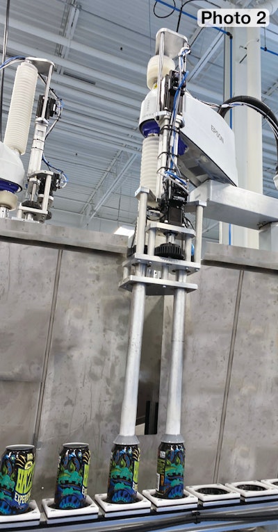 The end-of-arm tooling that picks cans from the rotating transfer wheel places both cans in the carriers of the servo-driven dual conveyor. Visible in the background behind the steel wall is a second robot that is putting cans into the dual conveyor’s other lane.
