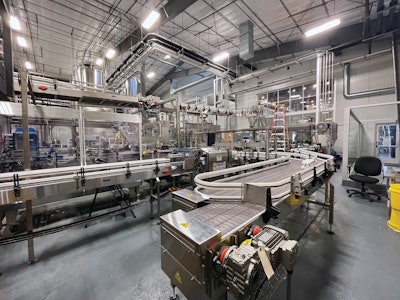 In this wide-angle photo of the packaging line, we can see an accumulation table ahead of a PakTech can handle applicator, Bevco conveyance, and a DMM case/tray packing in the background.