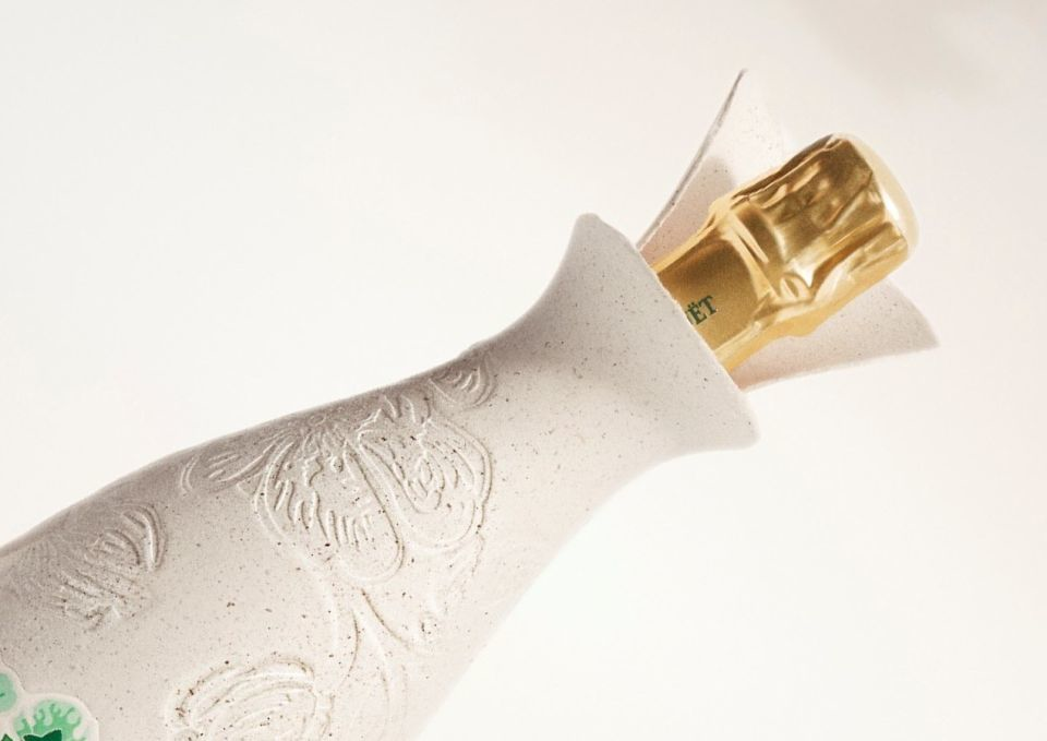 The Belle Epoque Cocoon exhibits an organic shape that gently enfolds the bottle. At the top, the golden cap of the bottle is revealed, surrounded by a petal-like, molded-pulp collar.