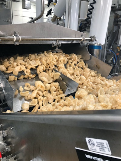 Product leaves the fryer and travels up a small incline conveyor to a vibratory distribution system on a mezzanine level, cooling as it’s carried.