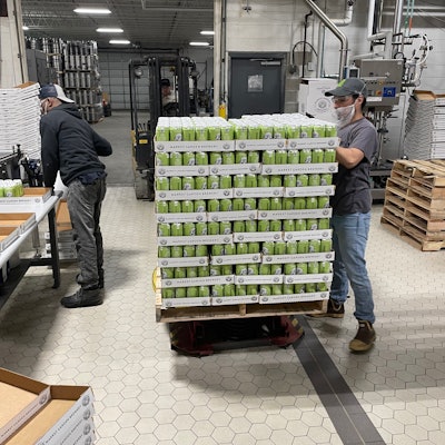 Operators pack out 24-count trays of can handle-applied 6-packs.