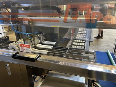 Capsules move through a series of laning mechanisms that guide them into three parallel lanes. Overhead starwheels index 10 capsules forward so that a push arm can advance 30 capsules per stroke into buckets that move off at a right angle.