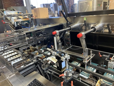 Capsules are pushed from buckets 10 at a time into cartons that are picked from a magazine feed. After cartons are erected and have their bottom flaps closed with adhesive, they’re filled and date coded before being closed and discharged.