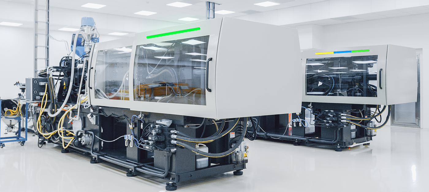 Industrial injection molding machines in a clean manufacturing facility with white walls and overhead lighting