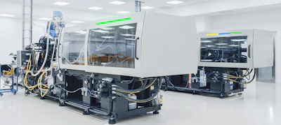 Industrial injection molding machines in a clean manufacturing facility with white walls and overhead lighting
