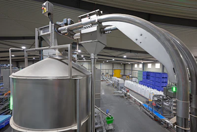 Industrial dairy processing facility with large stainless steel tanks and curved piping equipment in a warehouse setting