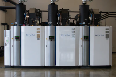 Three white Miura industrial boilers with black pressure vessels mounted on top in a facility