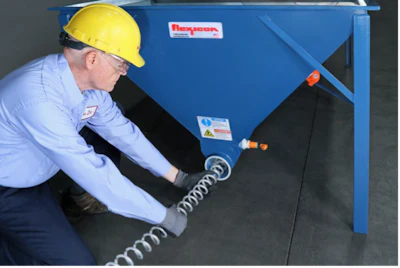 Technician in safety gear inspecting coiled hose on blue industrial hopper equipment