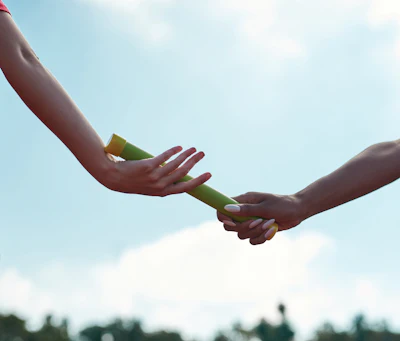 Two hands exchanging a green relay baton against a clear blue sky