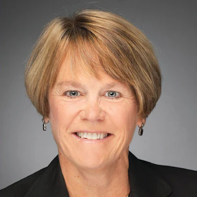 Professional headshot of a smiling woman with shoulder-length blonde hair wearing a black blazer and earrings