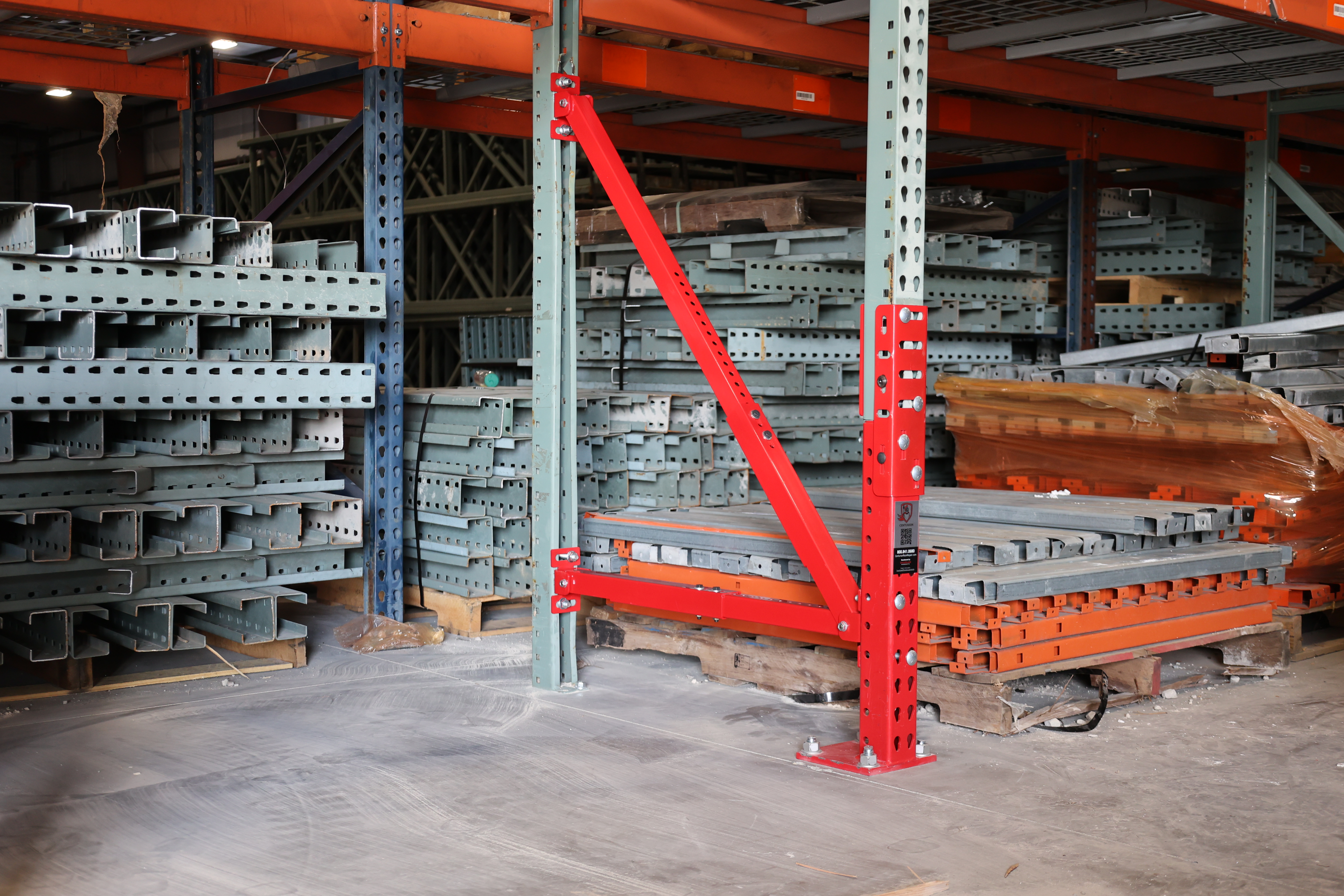 Industrial warehouse interior with orange and blue pallet racking systems storing metal components and red structural support beams.