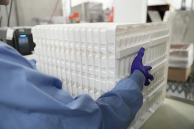 Worker in blue jacket handling white plastic crates with purple gloves in warehouse setting