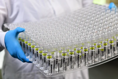 Laboratory technician holding a multi-well sample plate with yellow-green liquid samples during scientific testing