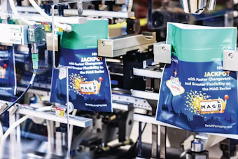 Industrial packaging equipment displaying MAG Series branded boxes in turquoise and navy with gold accents in a manufacturing facility