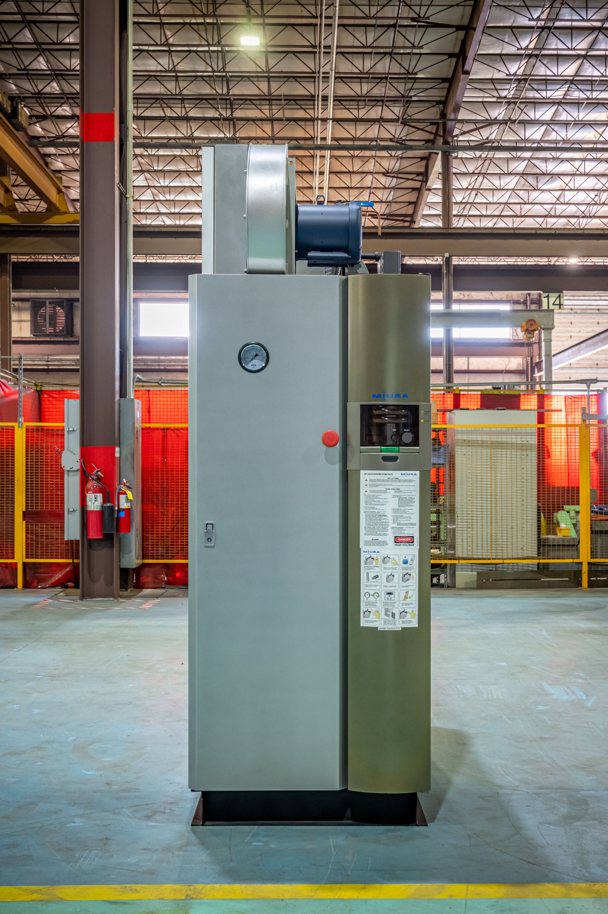 Industrial furnace or oven system with gray and olive-green panels in a warehouse facility with red safety barriers