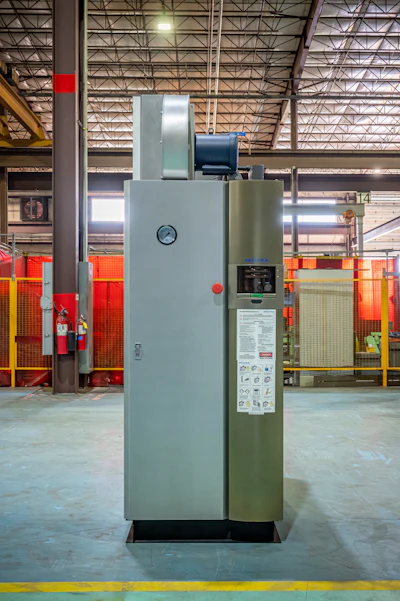 Industrial furnace or oven system with gray and olive-green panels in a warehouse facility with red safety barriers