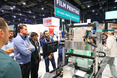 Trade show attendees examining industrial printing machinery at an exhibition booth with signage for film printing technology.