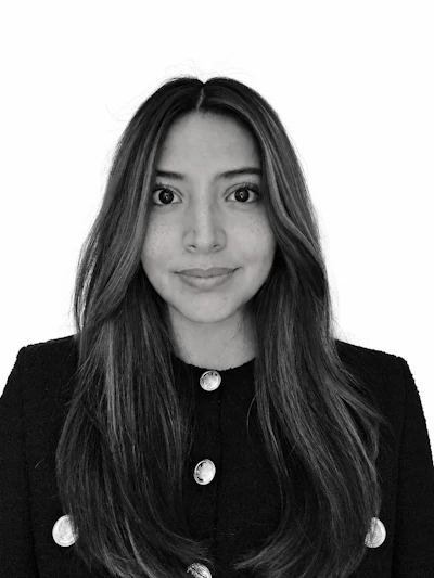 Professional black and white headshot of a woman with long dark hair wearing a black blazer with silver buttons