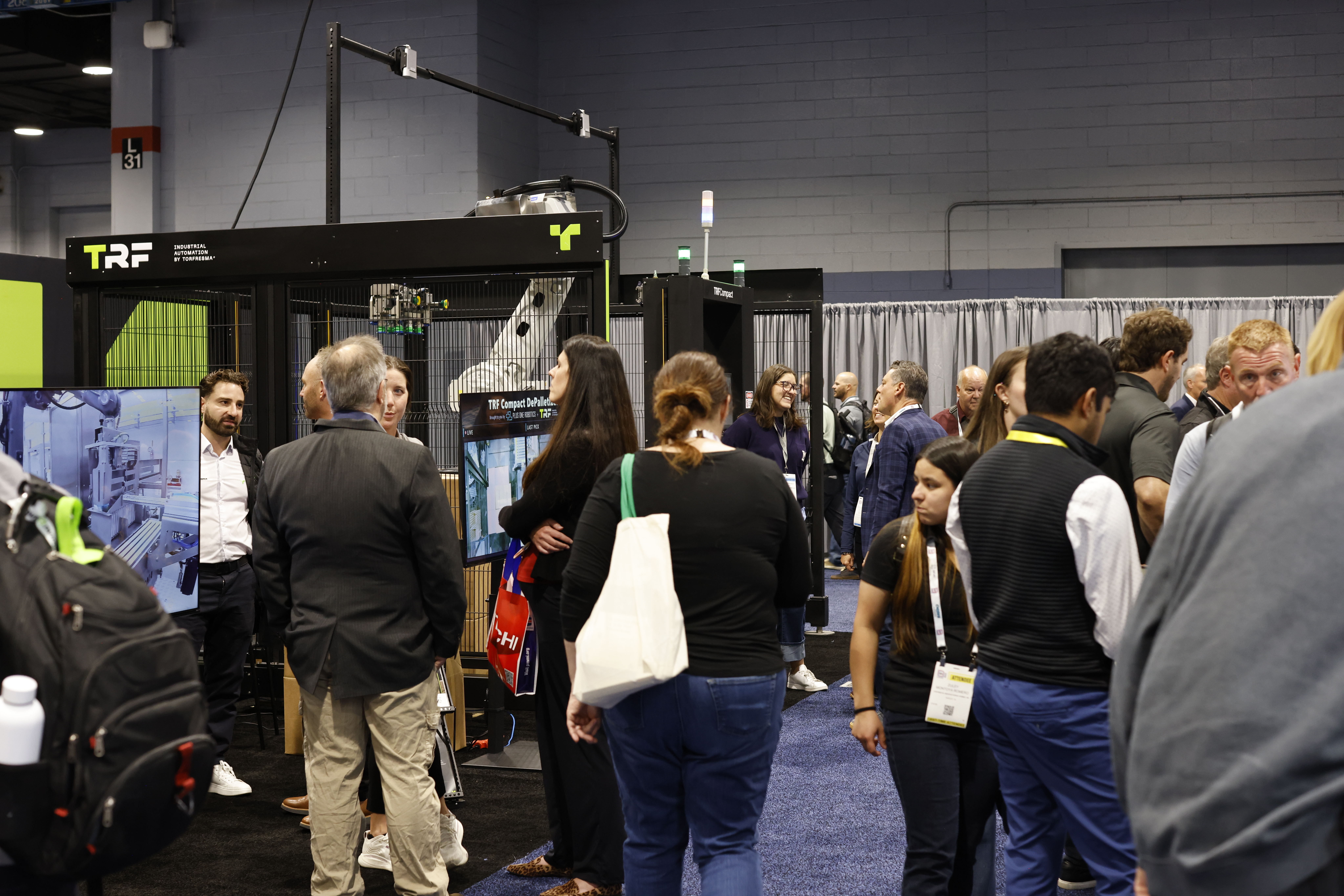 Attendees gather around exhibition booths at a trade show, with TRF branding visible on a black display booth featuring neon yellow accents.