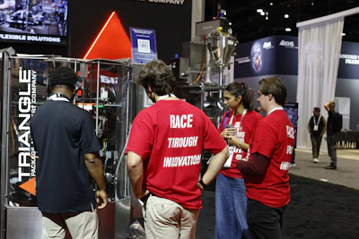 Team members in red shirts at trade show booth with Triangle company branding and neon signage