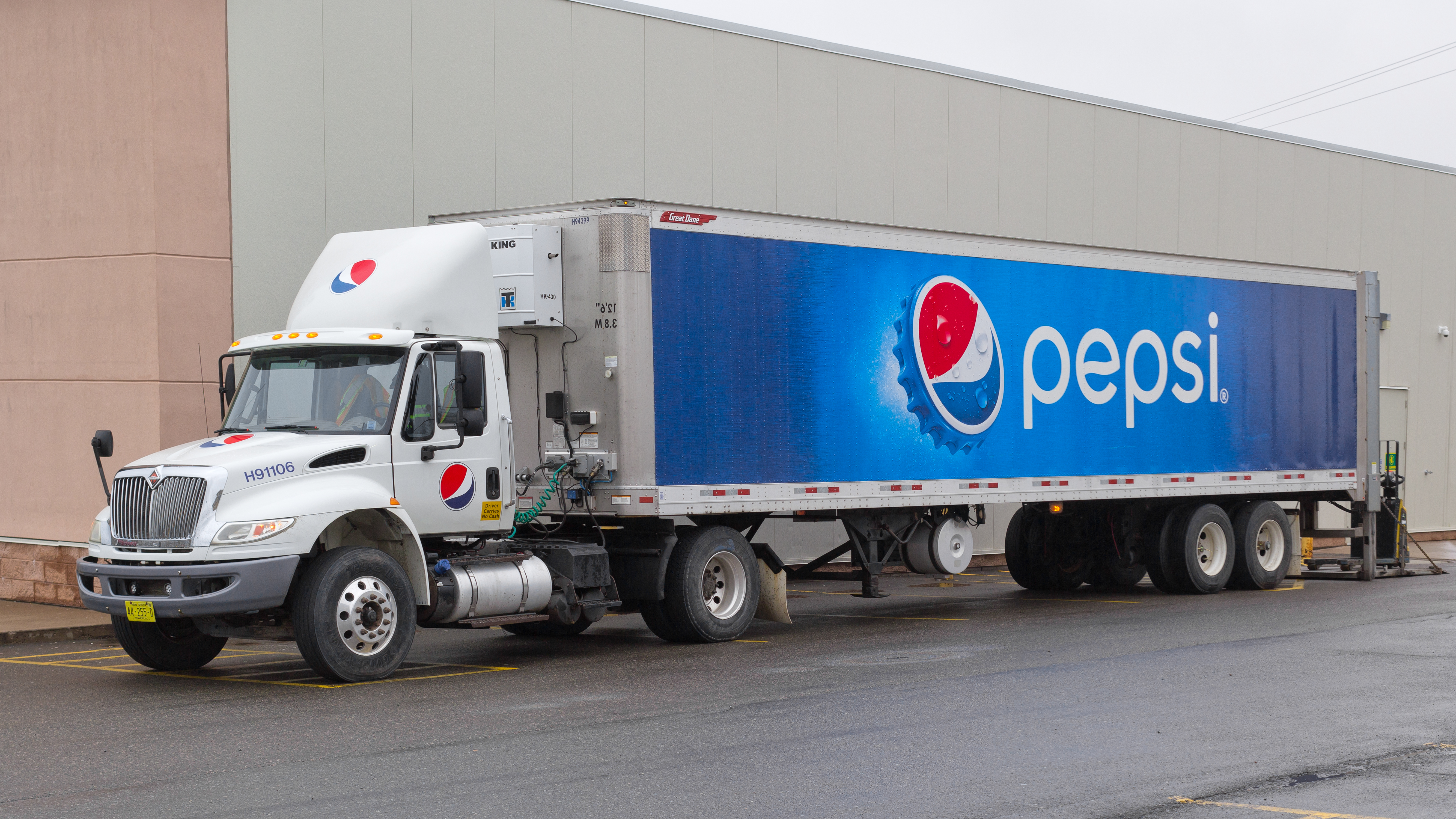 White Pepsi delivery truck with blue branded trailer parked against building