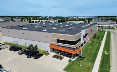 Aerial view of modern industrial facility with flat roof, orange entrance canopy, and VDC signage