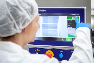 Operator in cleanroom suit using TOLEDO quality control inspection device displaying scan results and acceptance metrics