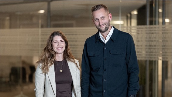 Two professionals smiling in a modern office hallway with glass walls